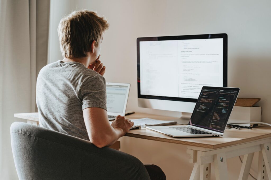 person sitting and thinking in front of three computers